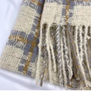 Close-up detail of soft winter plaid scarf texture, showing knit pattern and cozy fringe design.
