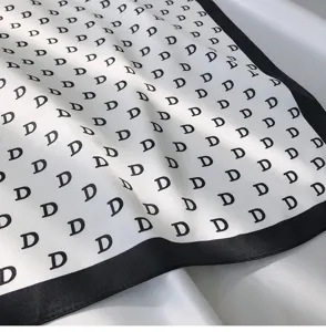 Close-up detail of a chic white and black square scarf featuring an all-over letter pattern.