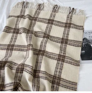 Close-up of cozy beige plaid scarf with chic fringe detail, soft fabric texture and warm style.