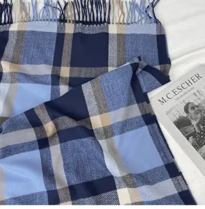 Close-up detail of soft blue and navy plaid winter scarf texture with elegant fringes.