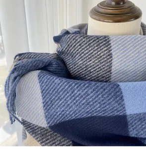 Close-up detail shot of the soft blue and grey plaid winter scarf fabric texture and tassel trim.