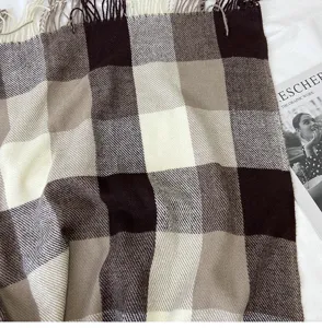 Detailed close-up of a cozy brown and beige plaid winter scarf featuring soft fringe ends.