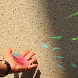 Detailansicht eines Kristall-Sonnenfängers in der Hand, der buntes Licht an die Wand wirft.