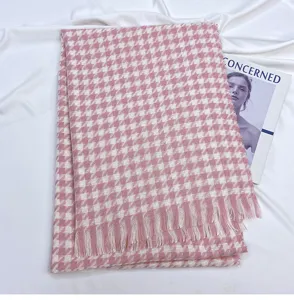 Detailed view of a pink and white houndstooth winter scarf with soft fringes and warm fabric.