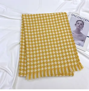 Detailed view of a yellow and white houndstooth winter scarf with fringe detail laid flat.