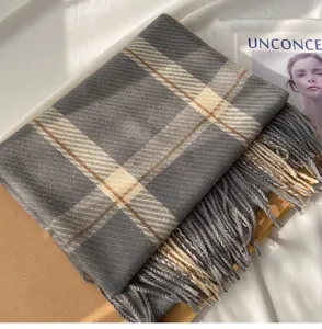 Detailed close-up of a cozy grey plaid fringed scarf displayed on fabric and props.
