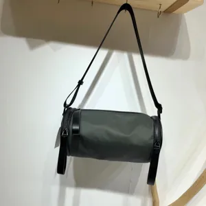 Detailed view of dark cylindrical nylon crossbody bag, showing its fabric and strap.