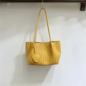 Close up of yellow soft woven leather underarm bag detail with cute heart charm accessory.