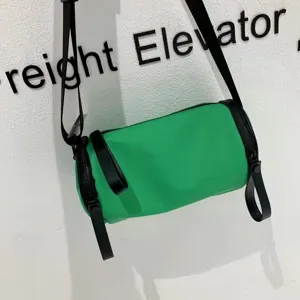 Green nylon cylindrical crossbody bag detail shot, compact barrel shoulder bag style.