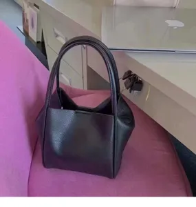 Detail shot of black pebbled leather bucket bag showcasing modern minimalist design on chair.