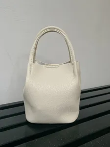 Vista dettagliata di una mini borsa secchiello in pelle crema, con dettagli di texture e manici.