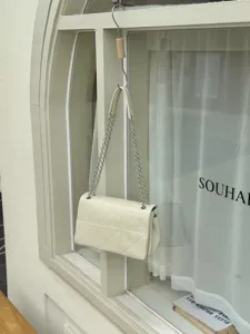 Detail view of chic white quilted shoulder bag with metal chain strap and elegant geometric design.