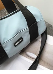 Light blue oxford cloth cylindrical crossbody bag detail view with black straps & logo patch