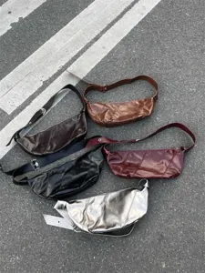 Detailed view of multi-color oil wax leather crescent shoulder bags arranged on pavement.