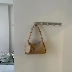 Vista dettagliata della borsa a spalla beige in morbida pelle con tracolla intrecciata e cuore.