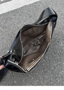 Detail view of black soft leather hobo shoulder bag with striped lining and wide strap design.