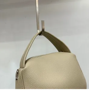 Close-up detail of beige leather lunch box handbag showing texture and top zipper design.