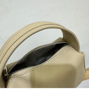 Close-up detail of beige leather handbag handle, metal zipper, and chevron inner lining.