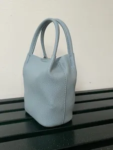 Vista di dettaglio della mini borsa a secchiello in pelle celeste con texture granulata e doppi manici.