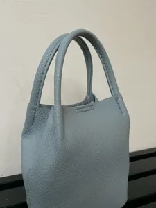 Vista dettagliata della mini borsa in pelle grigio-blu, con consistenza delicata e doppi manici.