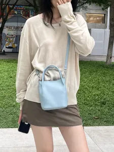 Primo piano di una mini borsa a secchiello in pelle azzurra indossata a tracolla.