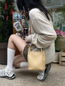 Primo piano della mini borsa a secchiello in pelle gialla, finitura testurizzata, accessorio chic.
