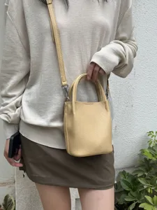 Dettaglio della mini borsa a secchiello gialla con texture in pelle e tracolla per donna.
