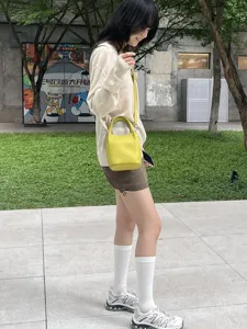 Primo piano di una mini borsa a secchiello in pelle gialla indossata da modella asiatica all'aperto.