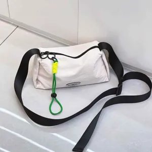 Detail view of casual white crossbody bag with wide black strap and green charm, close up.