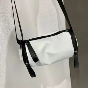 White cylindrical nylon crossbody bag detail, minimalist design with black strap.