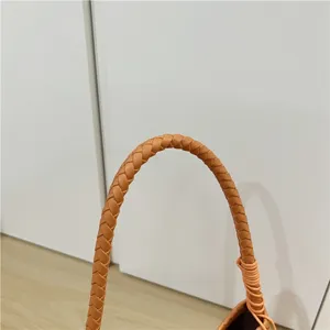 Orange woven leather handbag handle detail shot, stylish baguette underarm bag accessory.