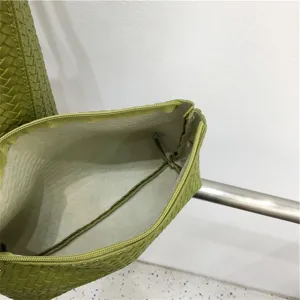 Green woven leather tote bag detail view, showing interior lining and zipper structure.