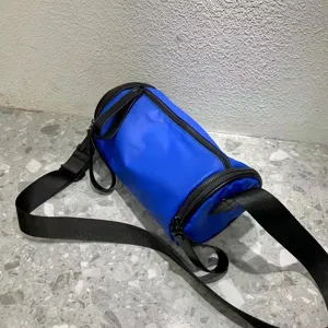 Blue nylon cylindrical crossbody bag detail shot, featuring durable black straps and zipper.