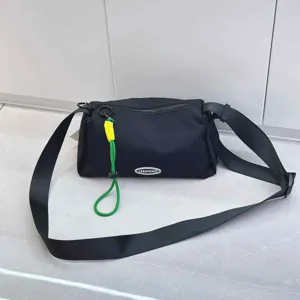 Detail view of the black nylon crossbody bag featuring green and yellow decorative rope charm.
