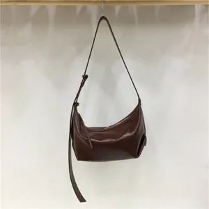 Detail view of minimalist glossy brown dumpling shoulder bag, hobo handbag strap close-up