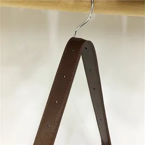Close-up detail of a minimalist brown leather bag strap with holes hanging on a wooden hanger.
