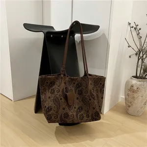 Detailed view of a brown suede tote bag with retro print, leather straps, and hanging pouch.