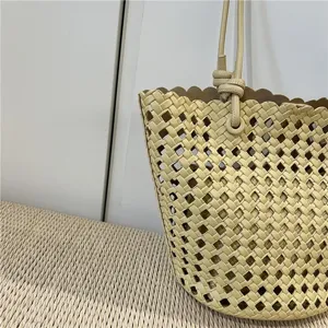 Beige woven leather bucket bag detail featuring hollow out lattice pattern and scalloped top edge.