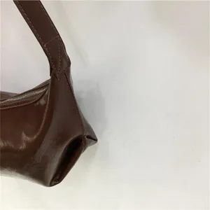 Close-up detail of dark brown glossy leather underarm dumpling shoulder bag side view.