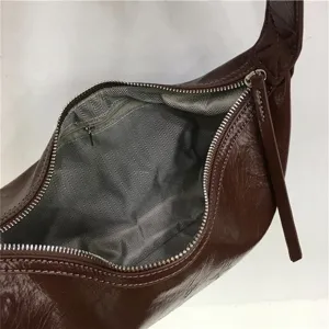Detailed view of the brown glossy dumpling underarm bag, showing smooth zipper and lining.