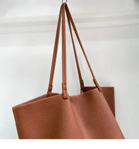 Brown leather tote bag detail showing soft pebble grain texture and long shoulder straps.