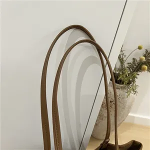 Detail shot of brown suede tote bag handle showing fine stitching and premium texture quality.