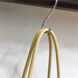 Detail view showing the fine leather texture and stitching of the stylish handbag handle hanging on a hook.