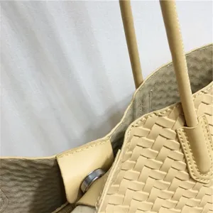 Close-up detail of soft woven leather tote handbag featuring double straps and buckle.