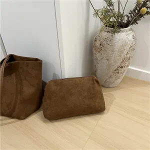 Detailed shot of brown suede tote bag and matching pouch on wooden floor with vase decor.