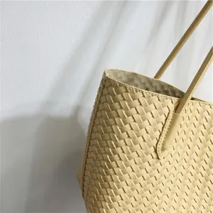 Close-up detail of beige woven leather tote bag, soft texture, elegant single shoulder strap.