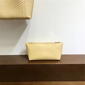 Minimalist solid yellow leather cosmetic pouch detail shot, compact daily makeup storage bag.