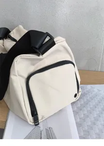 Close-up detail of casual beige duffel gym bag showing durable black strap and front zipper pocket.