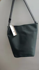 Dettaglio borsa a secchiello in tela grigia, tracolla in corda spessa con etichetta e logo.