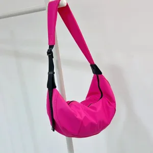 Bright pink nylon crescent dumpling crossbody bag detail, adjustable black strap, zipper.